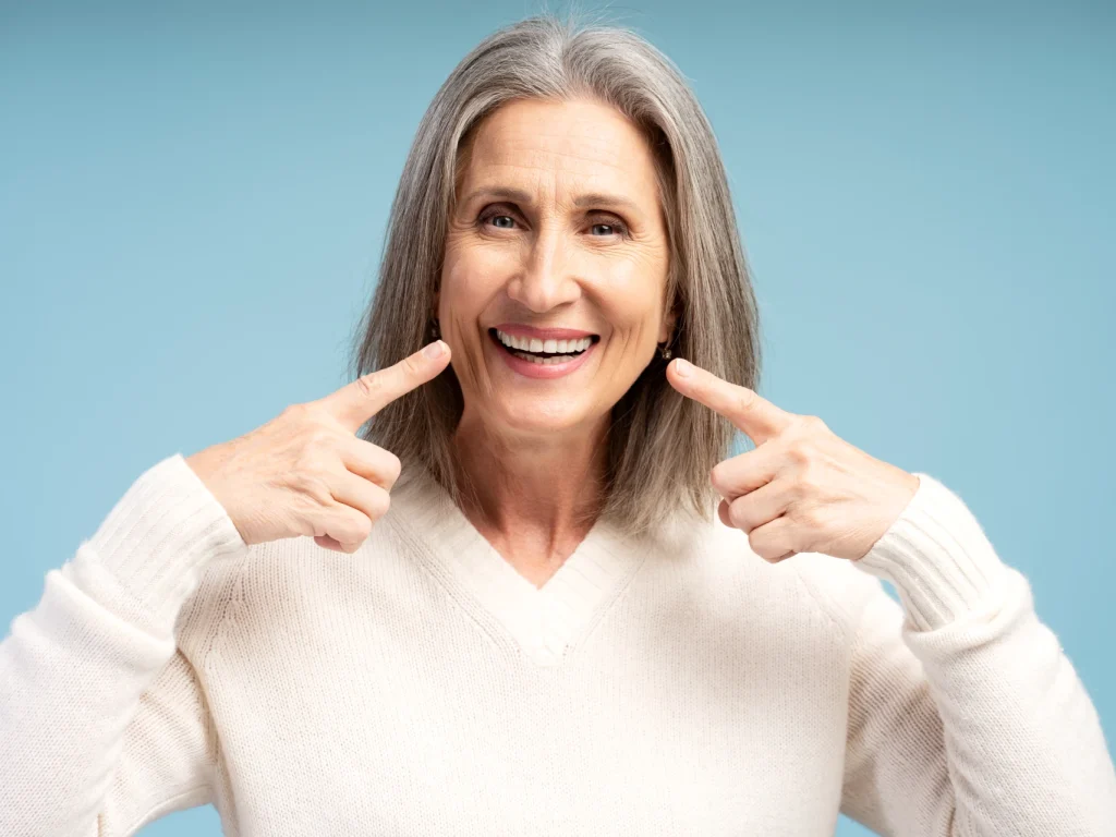 Senior woman smiling and pointing to her smile with both hands.