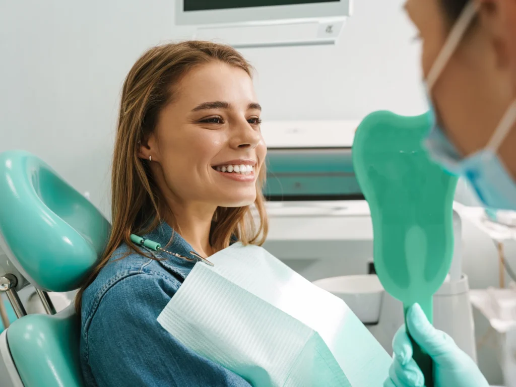 Young woman smiling in the mirror at the dentist after a teeth cleaning in Wilmington, NC.