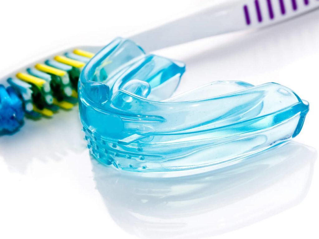 Up close photo of a blue plastic mouthguard and a toothbrush.