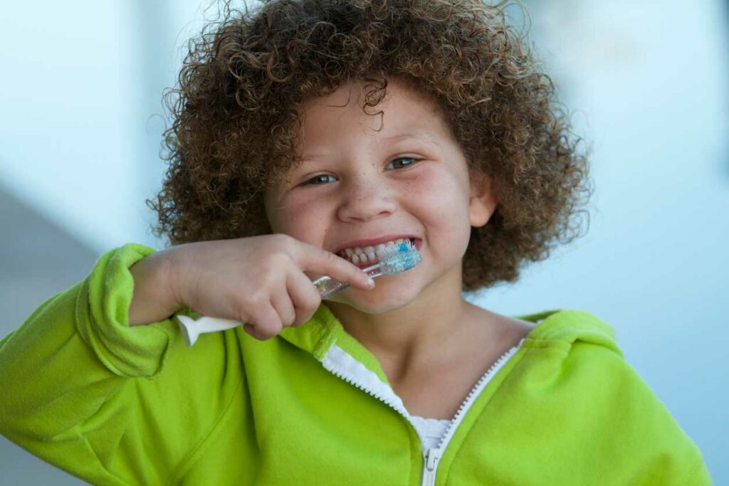Stock photo of a little boy wearing a green sweatshirt and brushing his teeth.