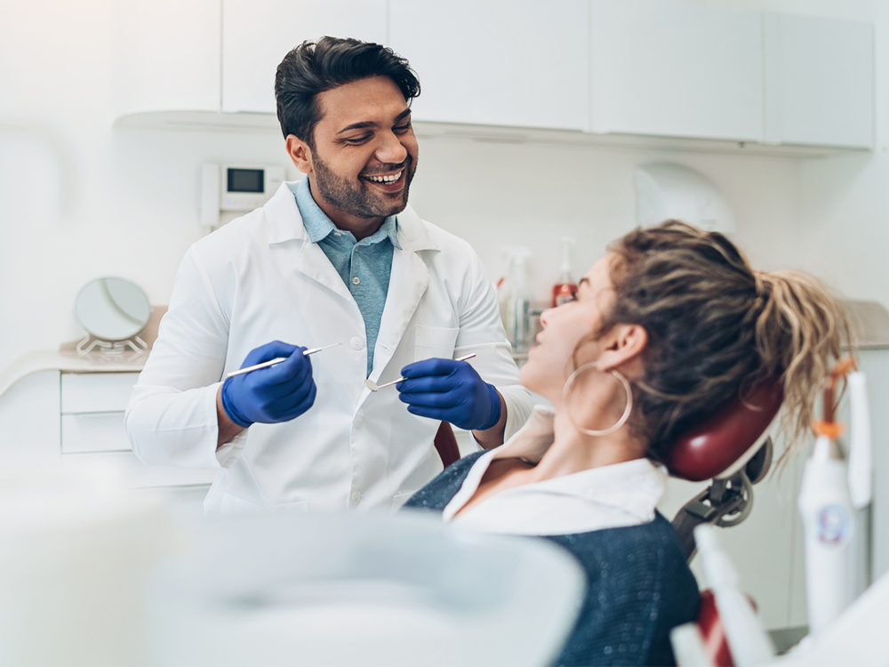Doctor holding dental tools while having chair-side conversation with a patient.